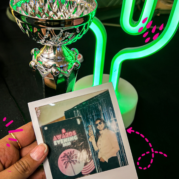 A hand holding a polaroid photo next to a trophy
