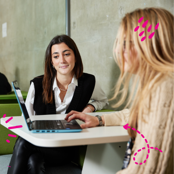 Two students sitting at a table with a laptop in the middle