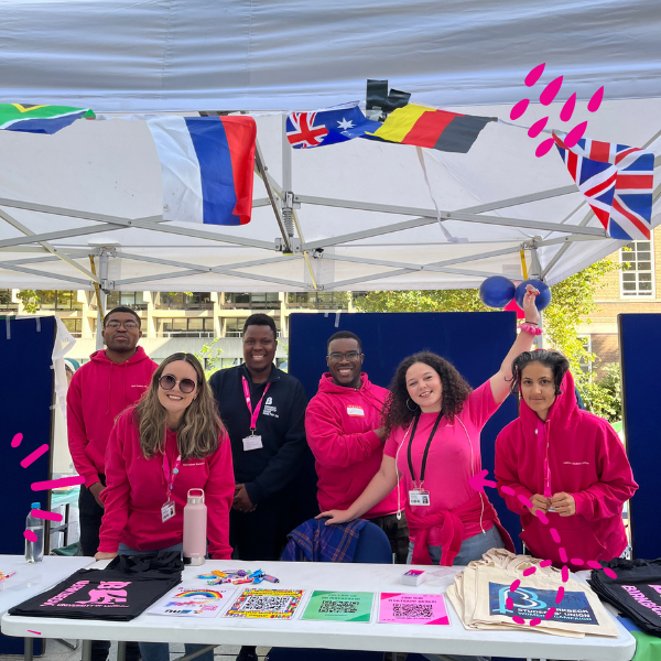 Photo of six students, smiling and with open arms wearing Birkbeck pink t-shirts at the Welcome Fair
