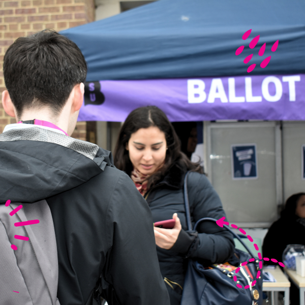 Image of a student talking to an other student, with a ballot station in the background