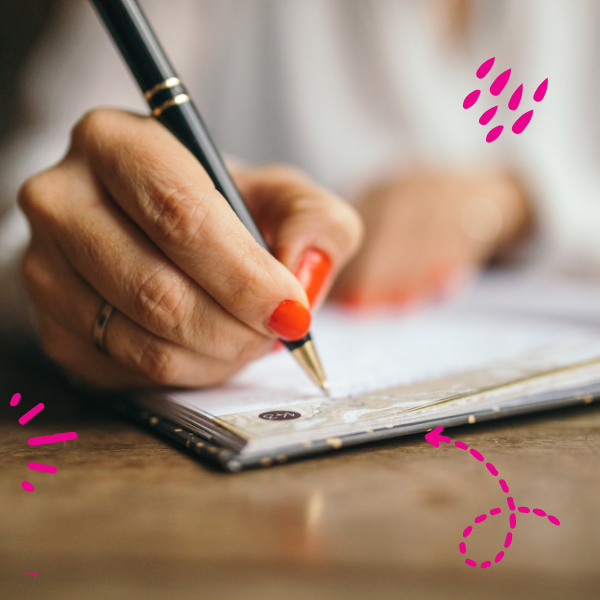 A hand holding a pen writing on a notebook